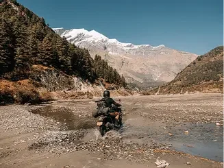Motorcyclist riding through shallow water in a Himalayan valley