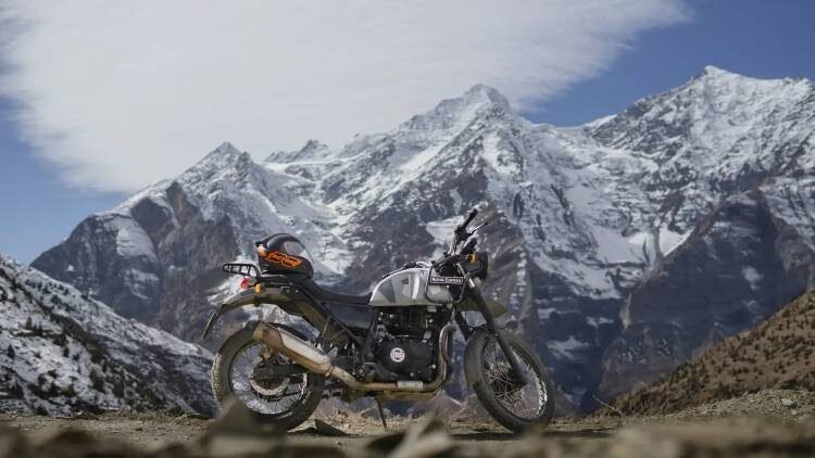 Royal Enfield Himalayan motorcycle parked in front of snow-covered mountains on a high-altitude trail