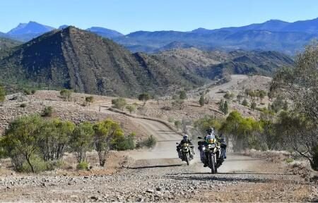 Two adventure riders cruising through a desert mountain trail in Oceania
