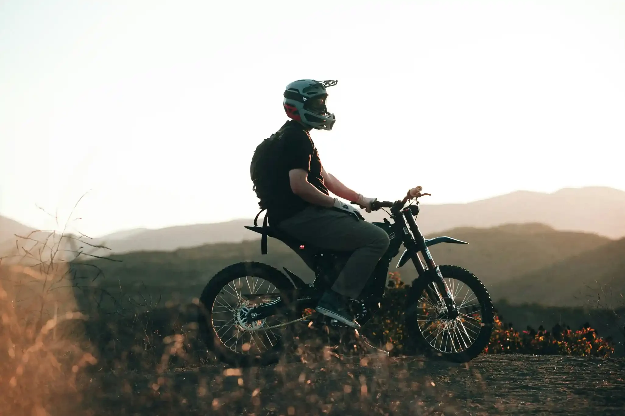 Rider resting on a dirt bike at sunset overlooking mountain hills