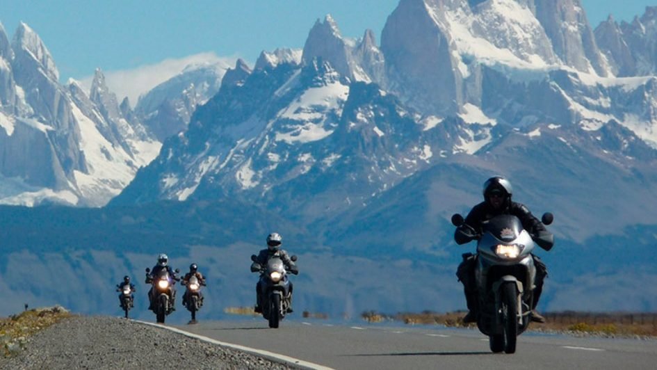 Motorcyclists riding towards the snow-capped peaks of Patagonia on a remote mountain road in Argentina.
